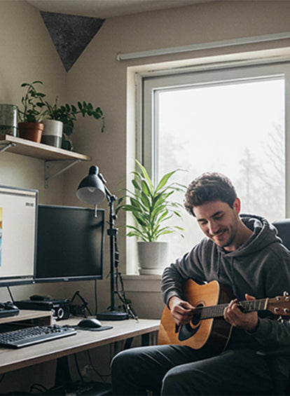 Man playing guitar in a home office with plants and a computer setup.